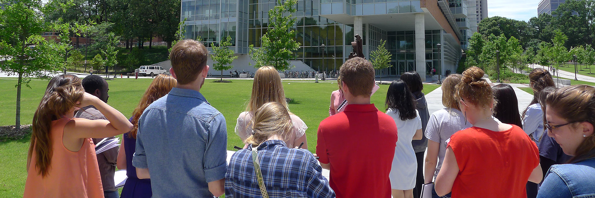 Visiting prospective students stand in front of the Architecture West building, looking at Clough Commons.