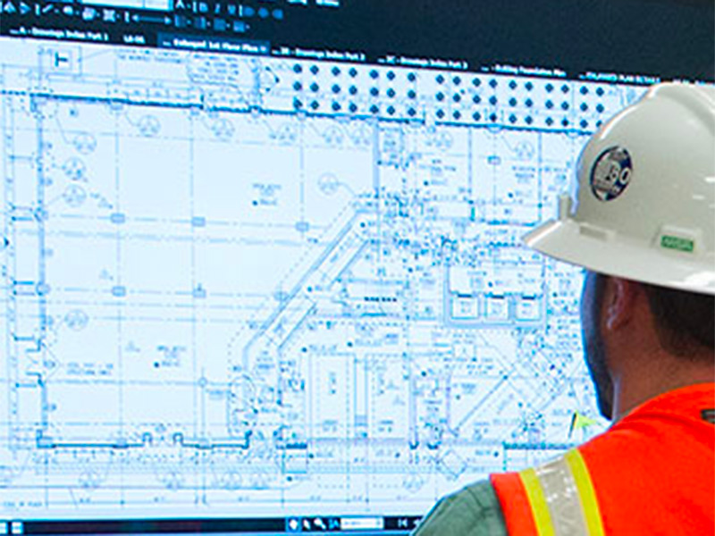 A construction worker looks at a screen showing building plans.