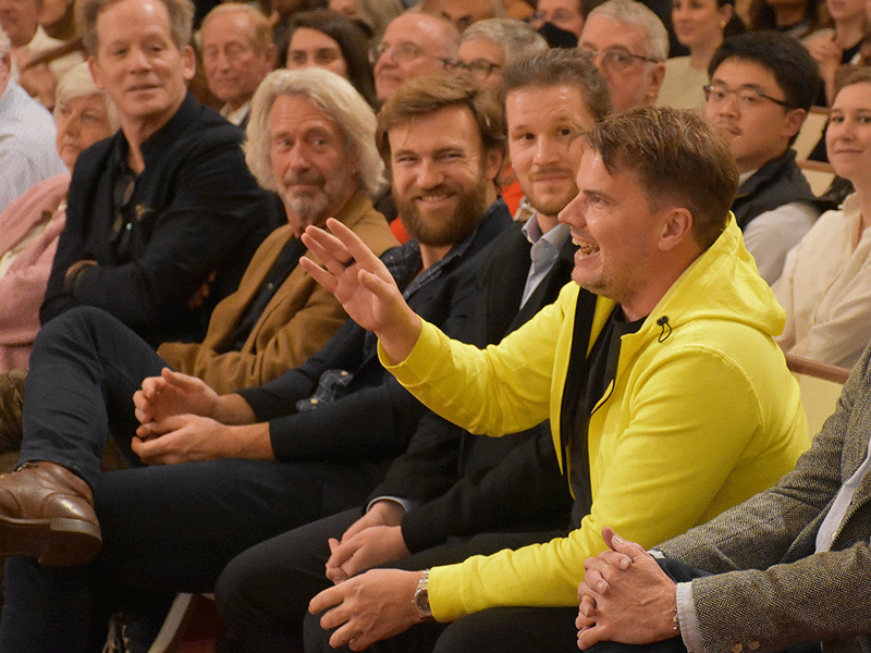 Bjarke Ingels in yellow hoodie seated with group of people