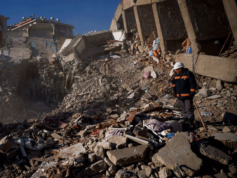 Man in safety gear examines rubble of collapsed building