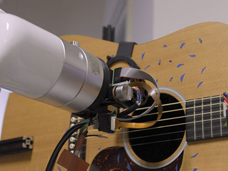 A robot arm strums a guitar