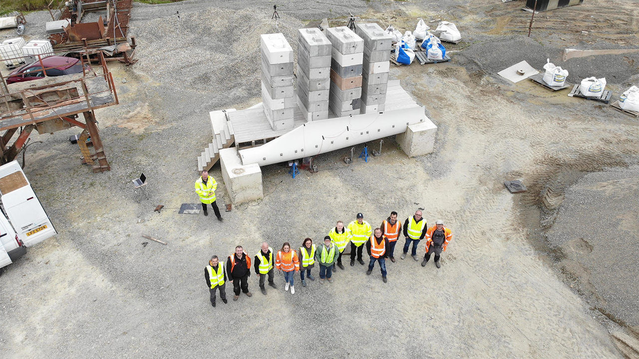 Aerial shot showing members of the Re-Wind Network stand in front of a pedestrian bridge made using decommissioned wind turbine blades