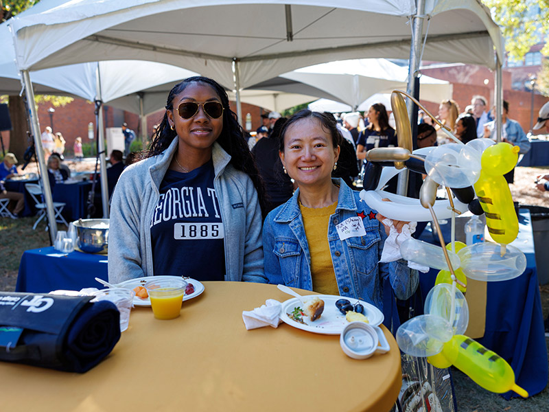 Alumni pose for a photo at a table with balloons