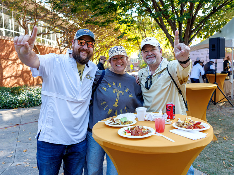 Alumni gather around a table, hold up "number one" fingers
